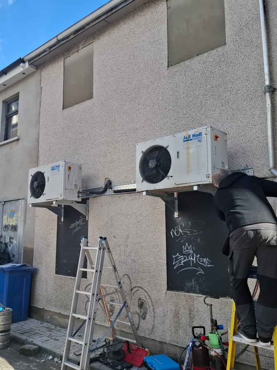 Fixall Services engineer working on wall-mounted commercial refrigeration condensers behind a bar