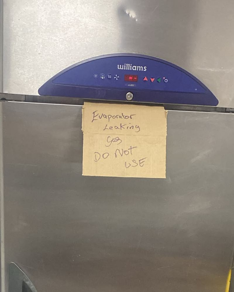 Commercial fridge tagged with a handwritten note reading evaporator leaking gas, do not use